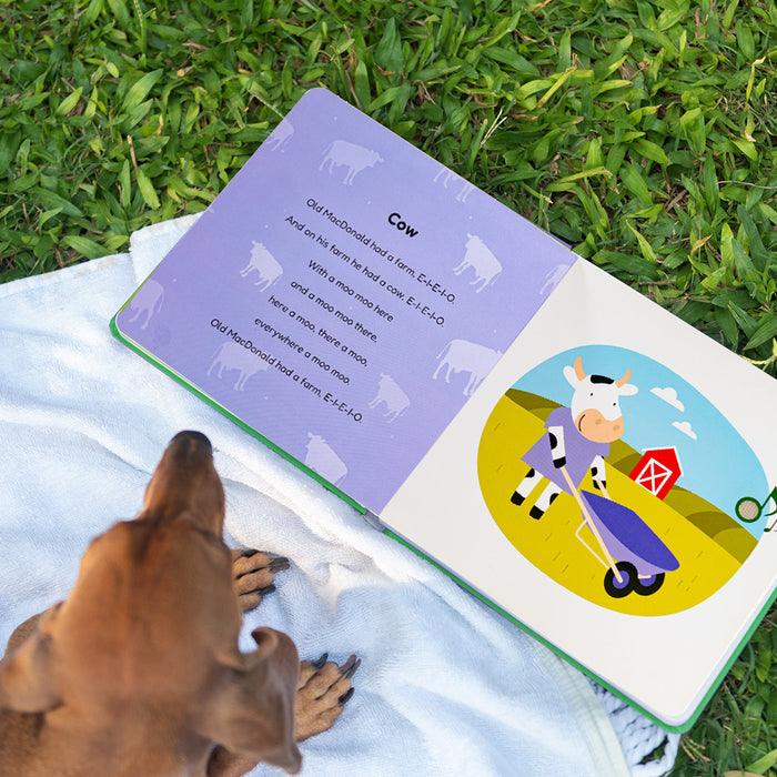 A dog is sitting next to a sound book laying on the grass. Musical books for kids, toddler musical activities, kids learning, toddler education.