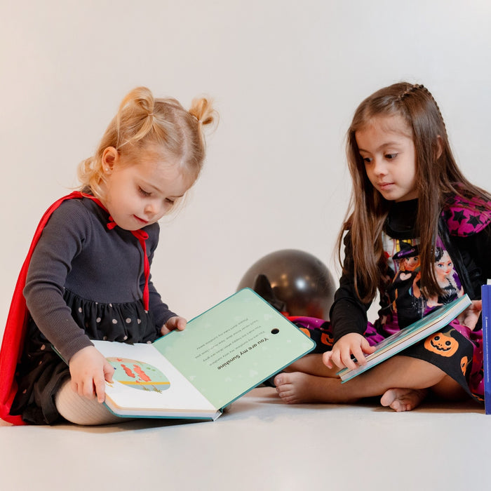 Two girls dressed as witches are sitting down and reading picture books. Halloween books, halloween activities, halloween tips, kids books, kids reading.