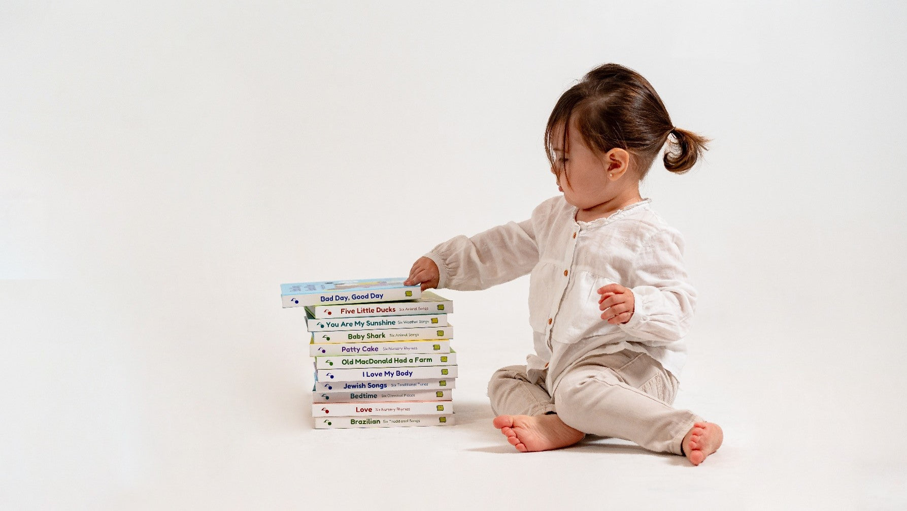 A toddler girl is touching a pile of sound books. Picture books, musical books, kids books, bedtime books.